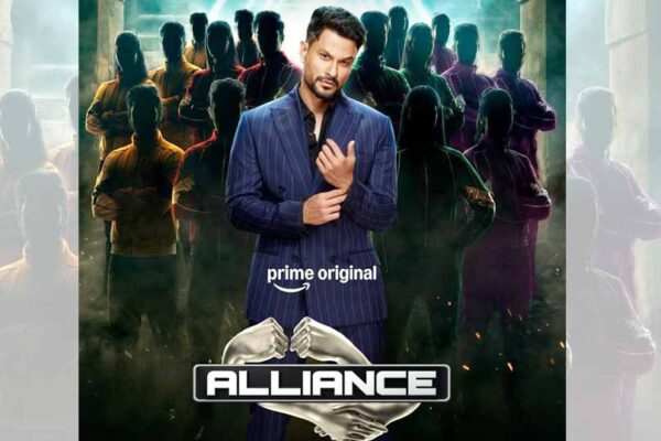 प्राइम वीडियो की रियलिटी सीरीज़ "Alliance" का आधिकारिक पोस्टर, जिसमें होस्ट के रूप में कुणाल खेमू नीले सूट में दिखाई दे रहे हैं और उनके पीछे कई प्रतिभागियों की परछाइयाँ नजर आ रही हैं।